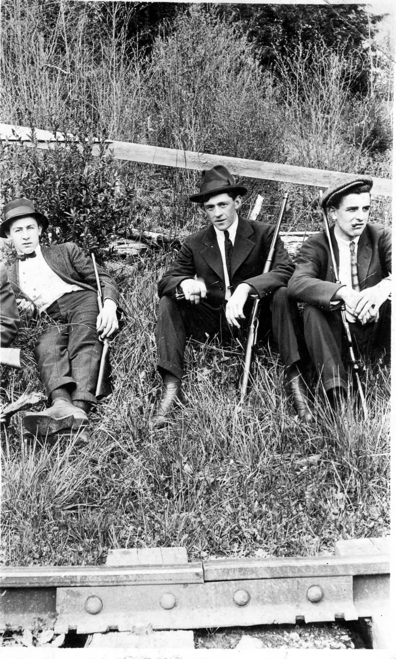 Three men hold guns while dressed in their Sunday attire 