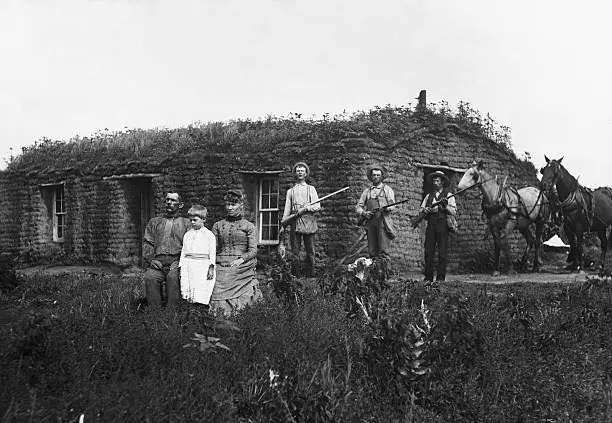 A family poses in front of sod house