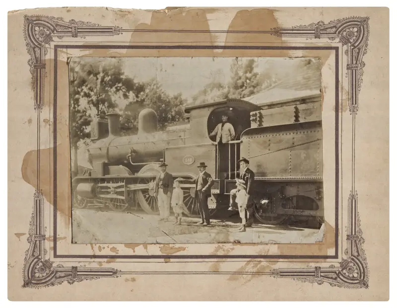 Grupo de hombres y niños juntos a una locomotora del Ferrocarril del Sud