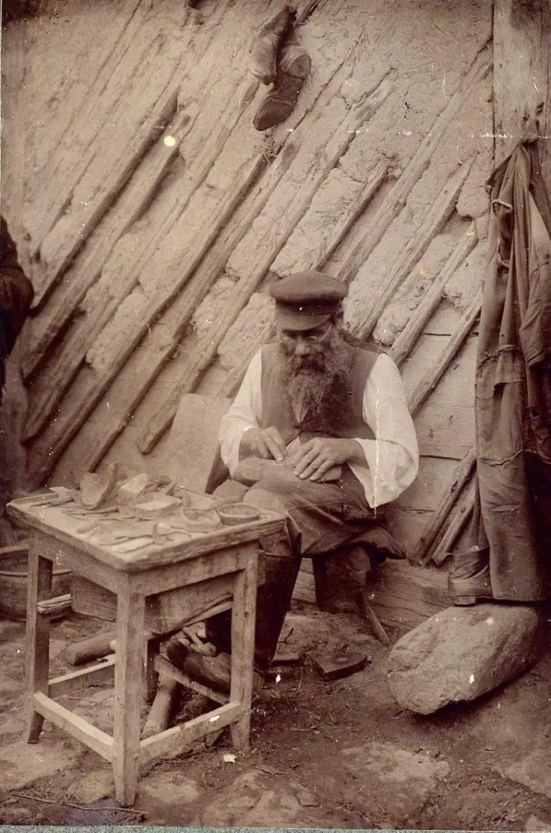 A shoemaker at the wall of the house at work