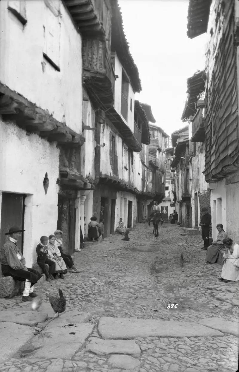 Vista de una calle, con los vecinos sentados en las puertas de las casas.