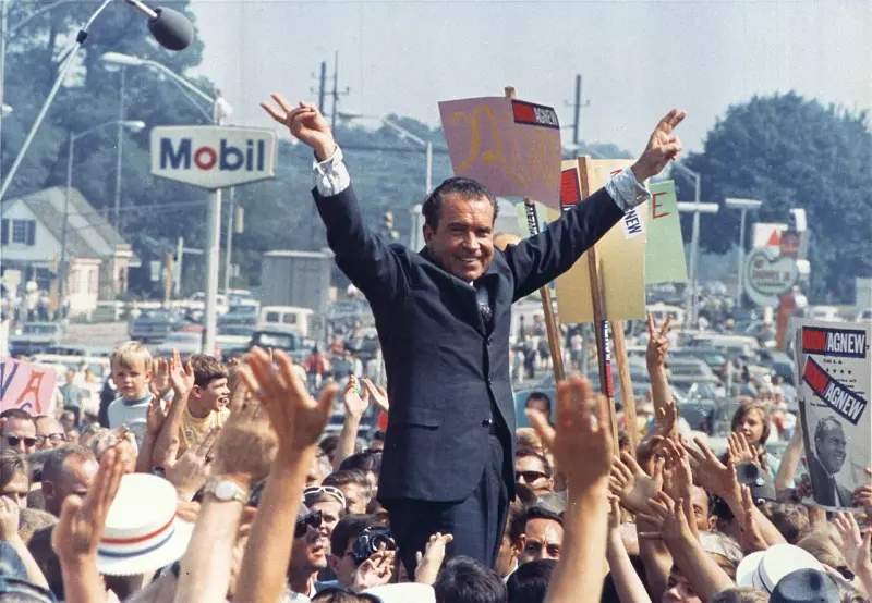 Richard Nixon gives his trademark "victory" sign