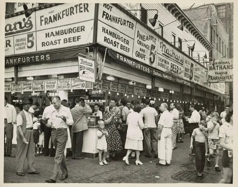 People eating sausages in buns outside Nathan's Famous fast food restaurant