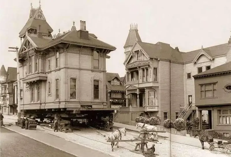 A Victorian home being moved via horse power.