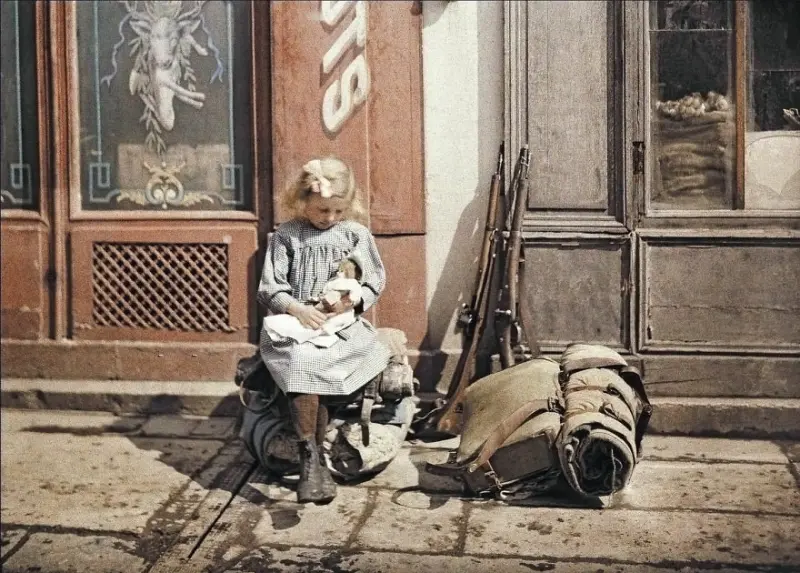 Girl playing with a doll next to her father's equipment on a street in Reims